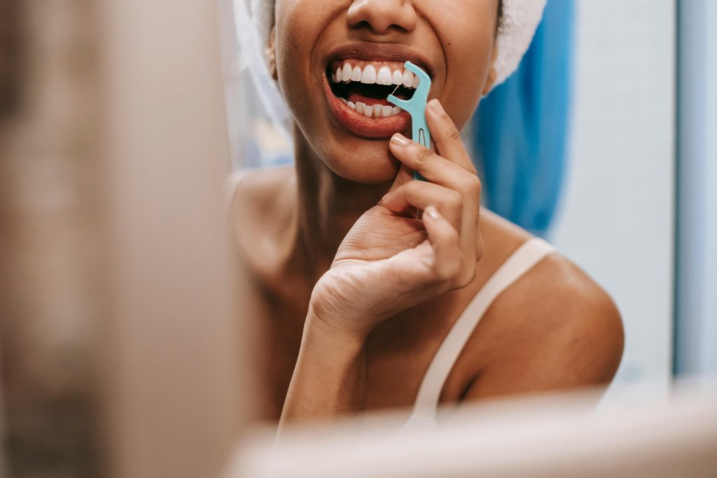 Young African American woman practicing oral hygiene by flossing teeth in front of a bathroom mirror.